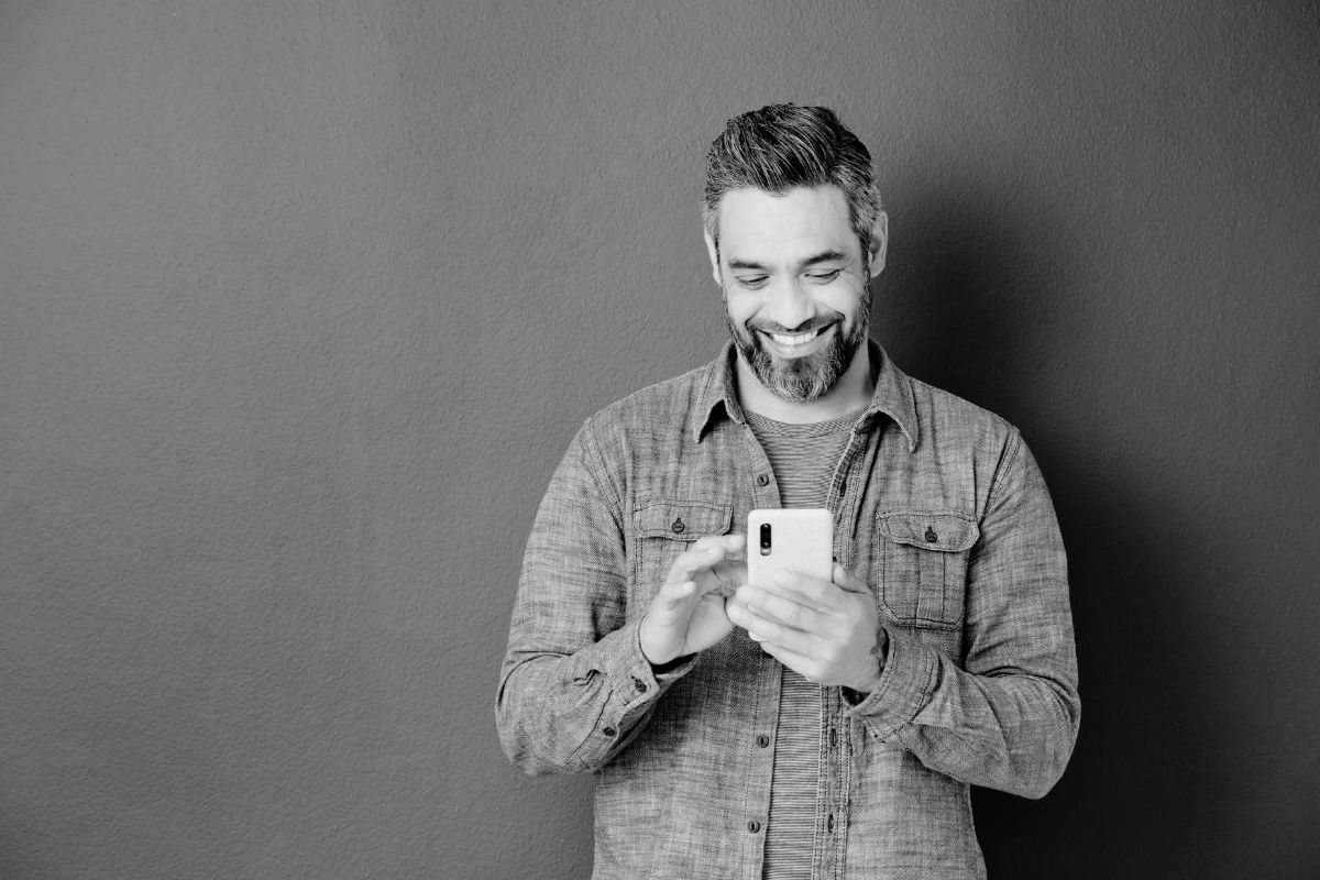 Un hombre sonriente sostiene un teléfono celular en su mano, mostrando alegría y conexión con la tecnología.